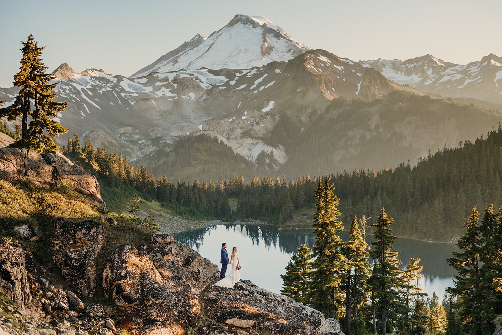 A couple stands watching sunset with Mt baker behind them.