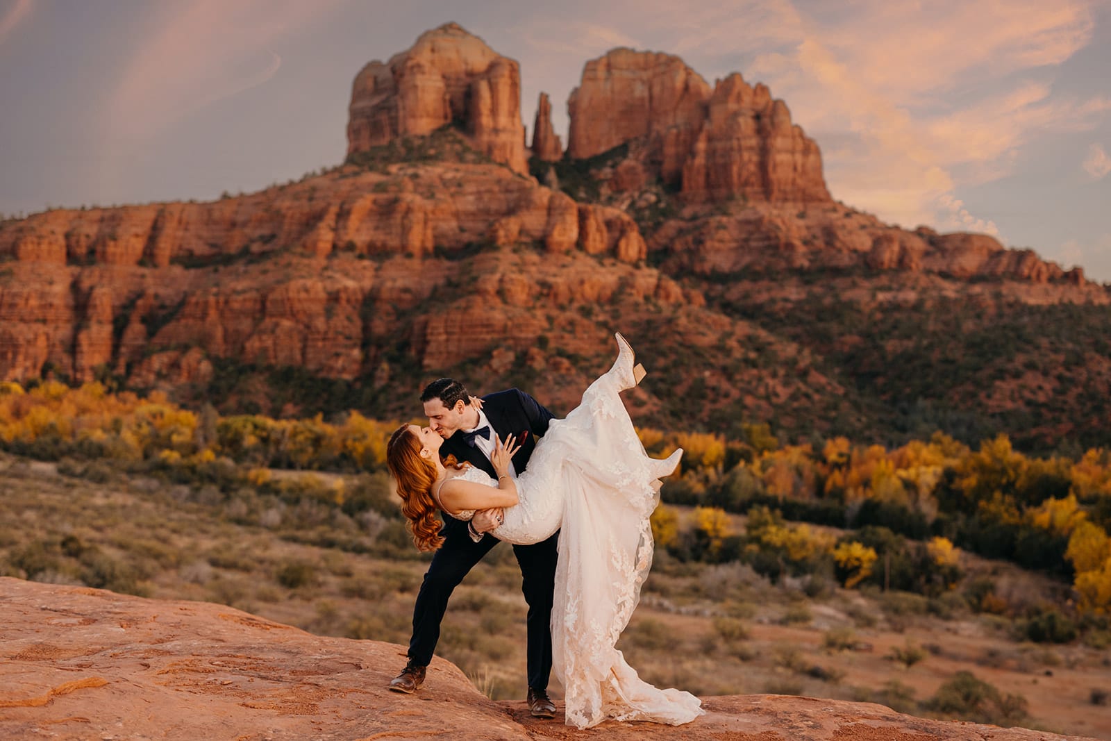 A groom dips his bride back for a kiss in front of Cathedral Rock.