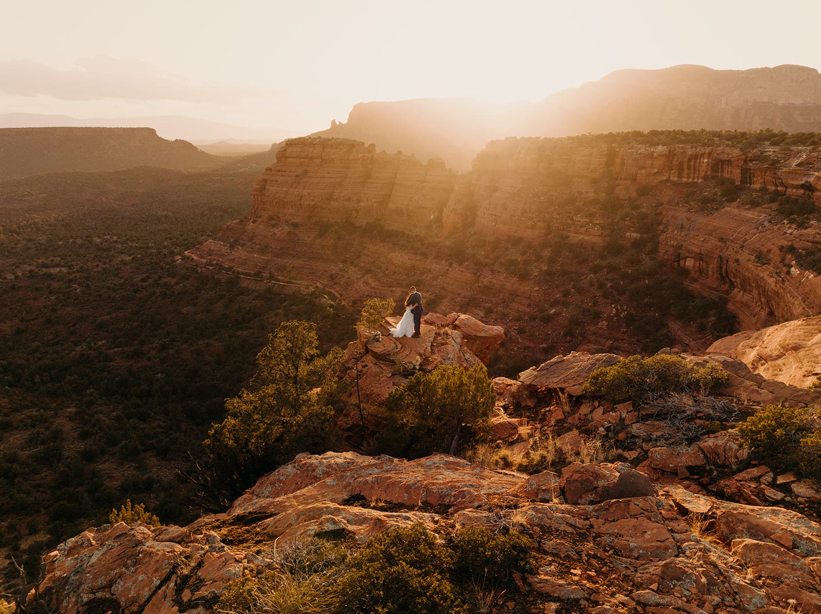 A couple stands out in the distance on a cliff edge at sunset in Sedona.