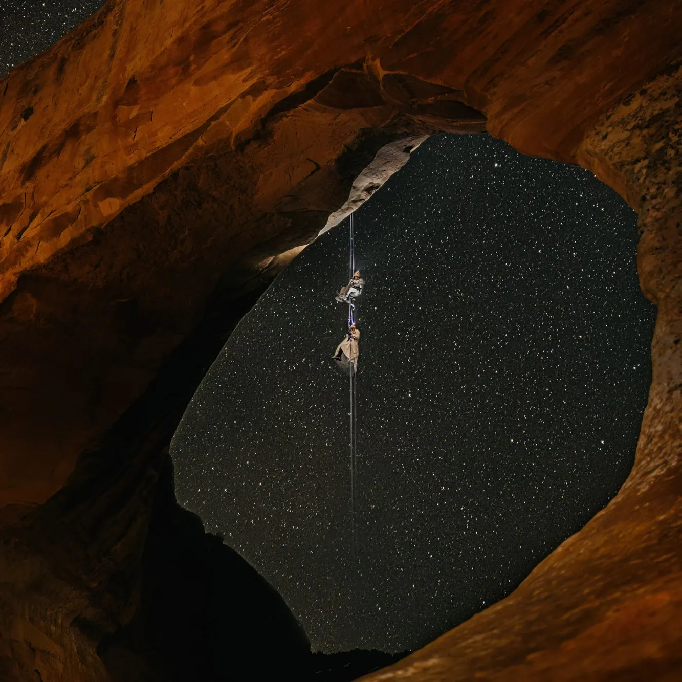 A couple rock climbs under the stars on an arch in Moab.