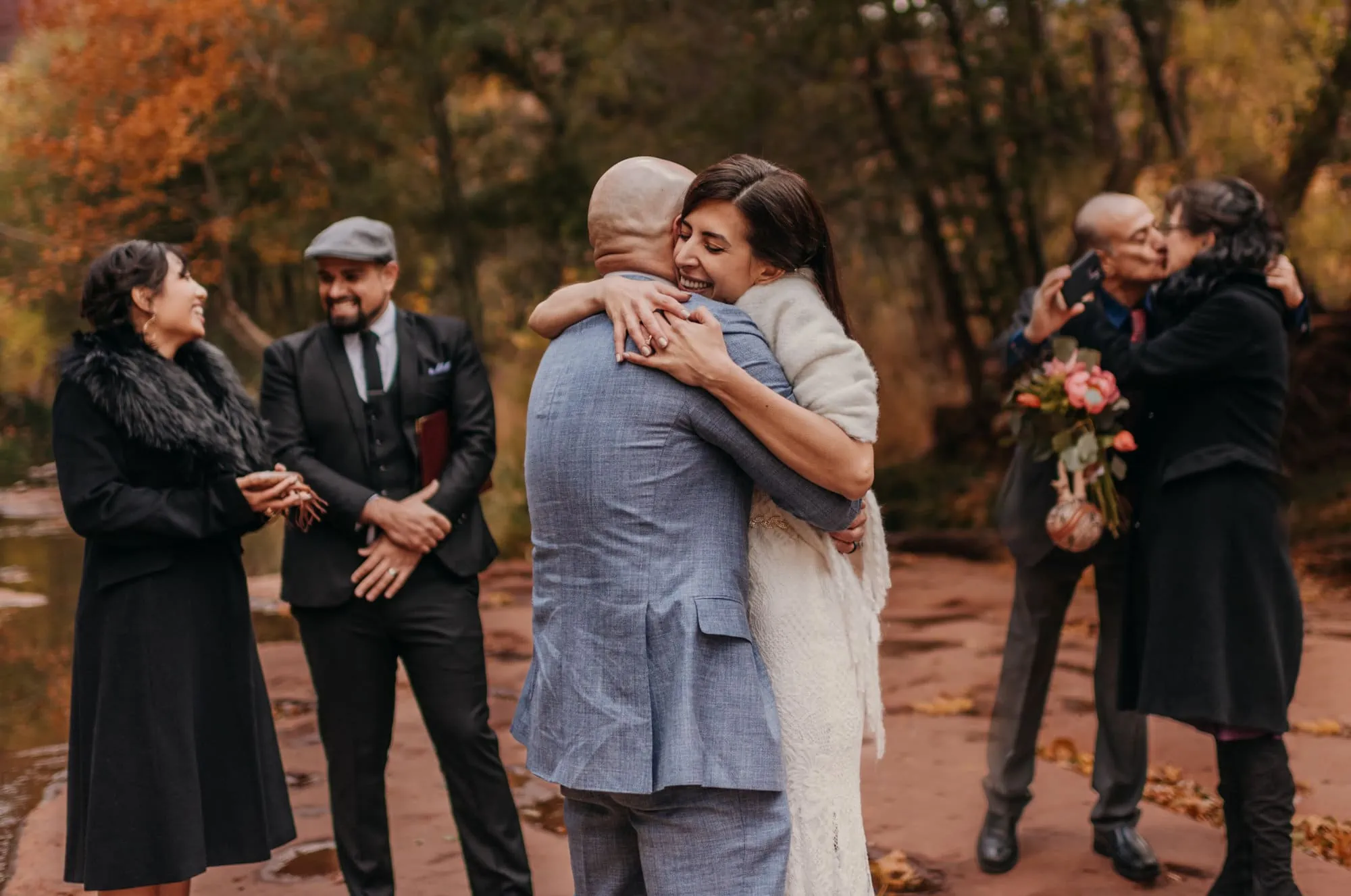 A bride and groom hug after being announced married and their guests embrace each other. 