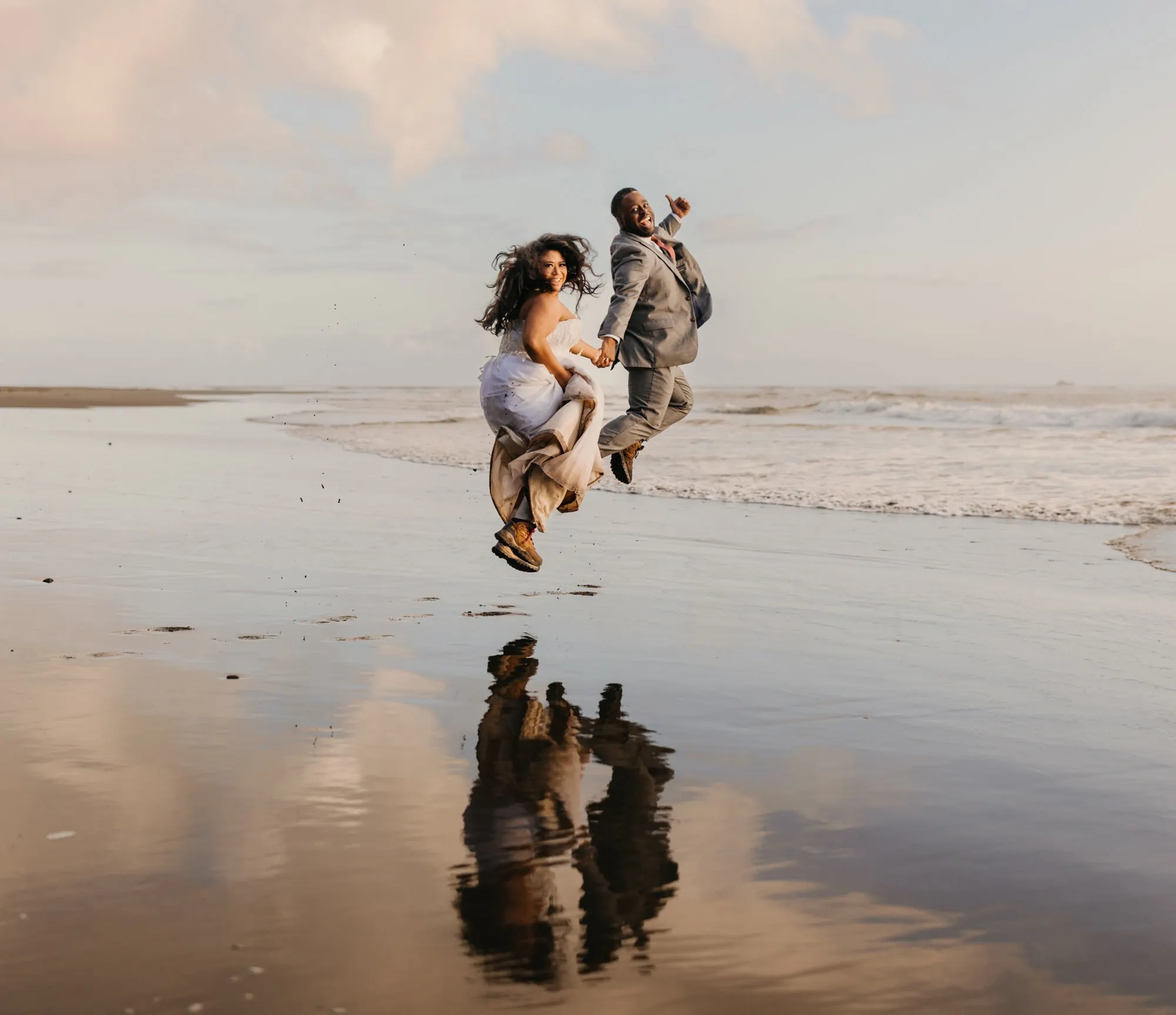 A bride and groom leap in joy on the coast line. 