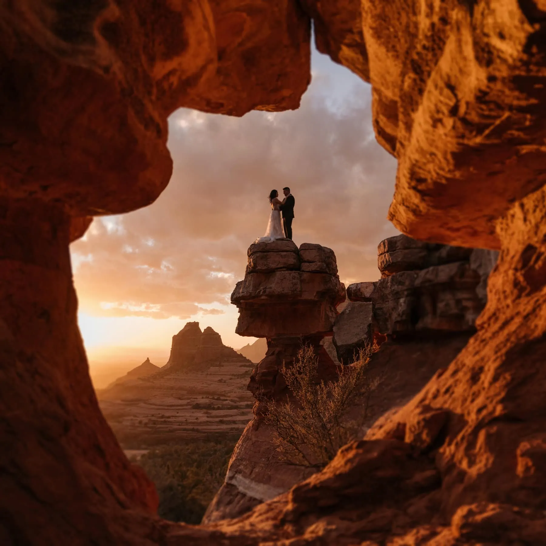 A photo through a keyhole cave of a couple standing on a ledge.