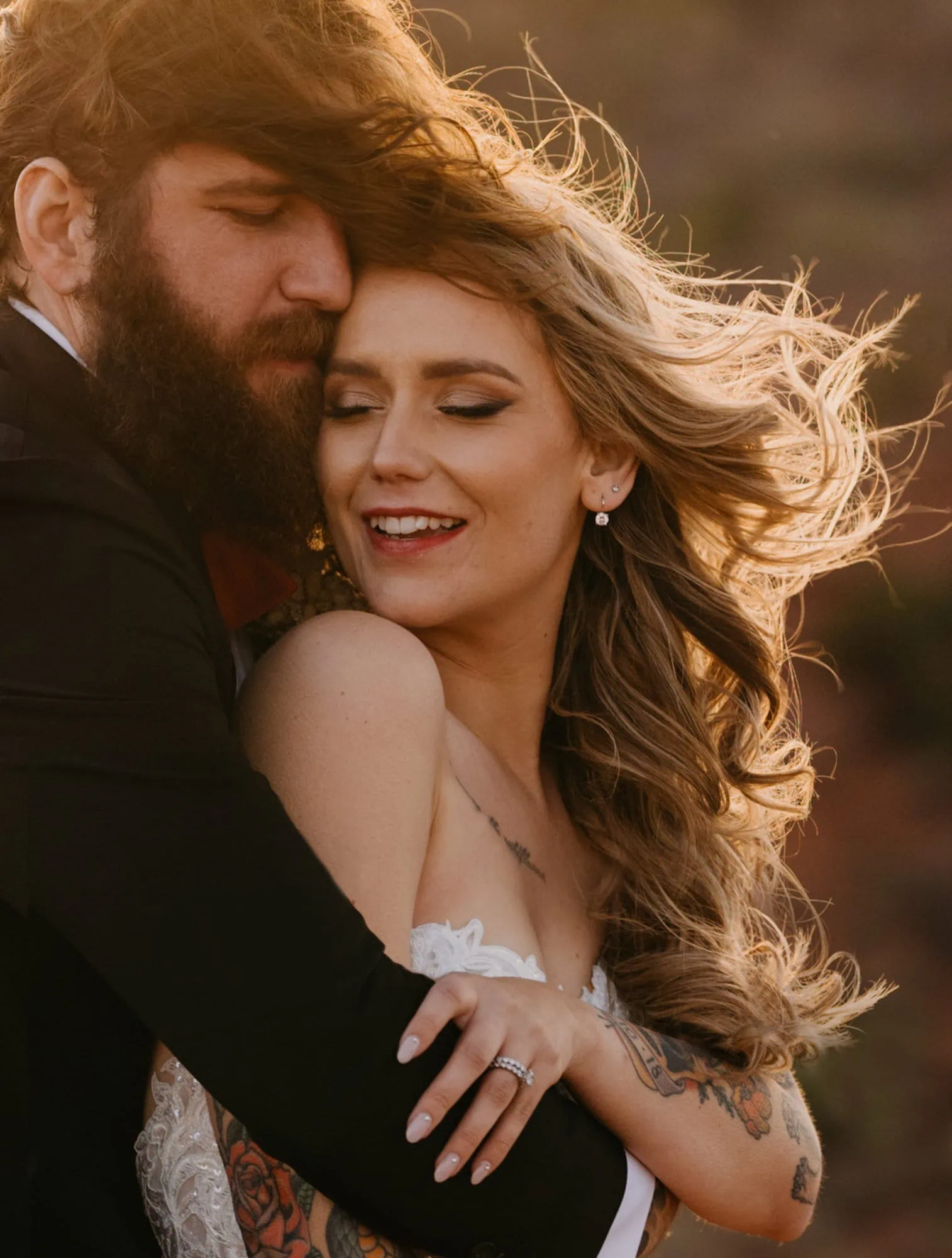 A bride holds her groom as wind sweeps their hair together.