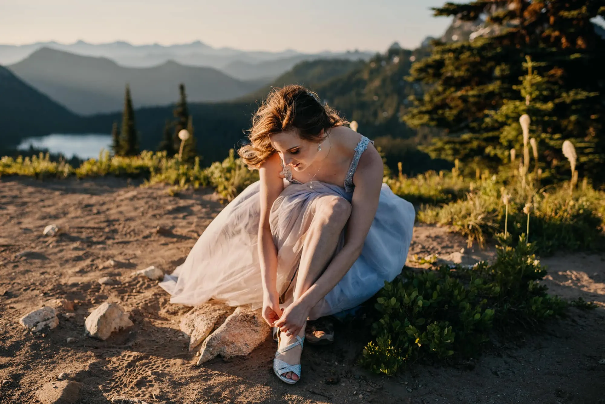 The bride ties her shoe while sitting on the trail.