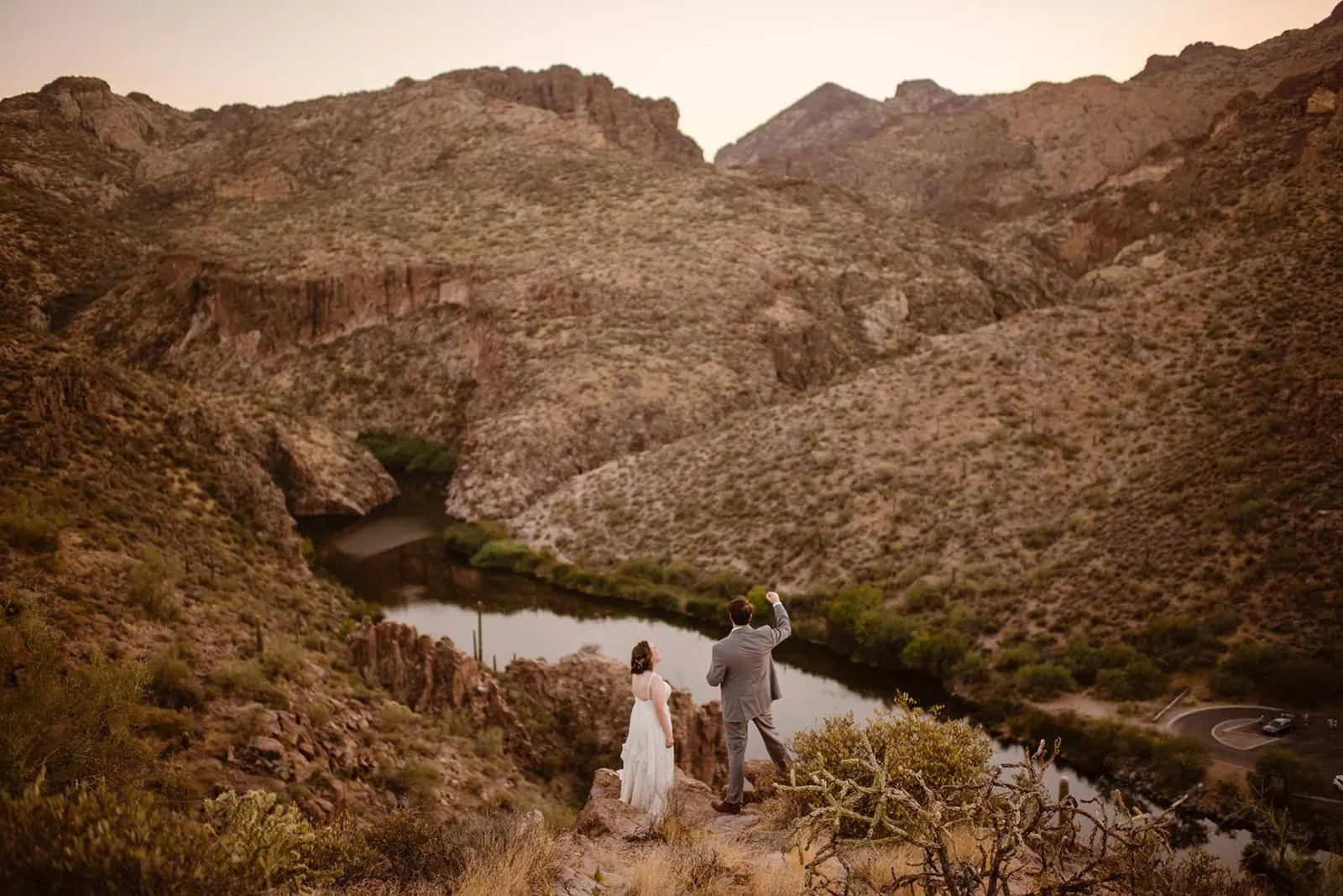 A groom celebrates his marriage on the edge of a cliff in Phoenix's Superstition Mountains at dusk.
