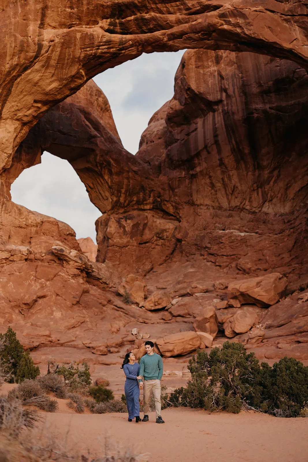 A man and woman stand together under double arch in arches national park.