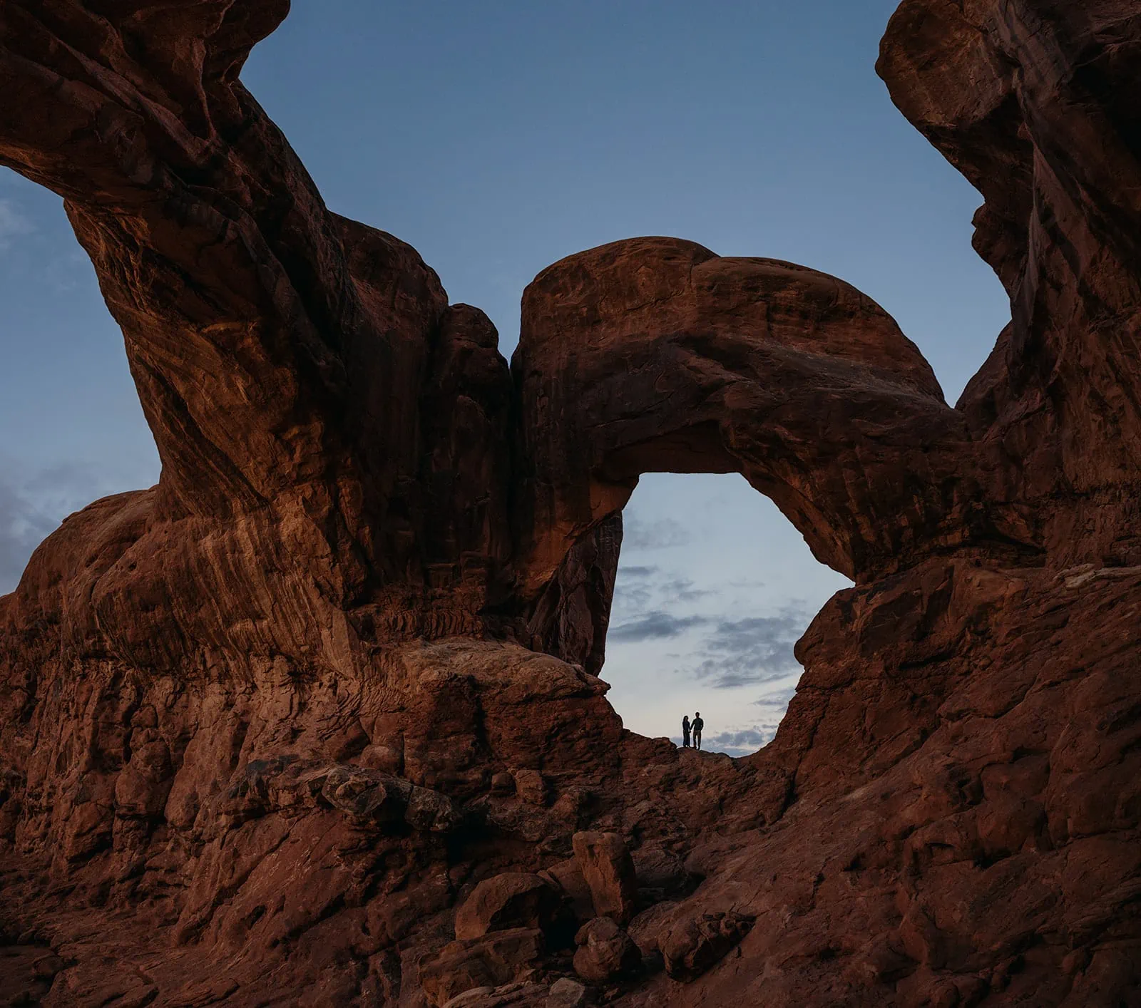 A man and woman stand together within an arch at sunrise