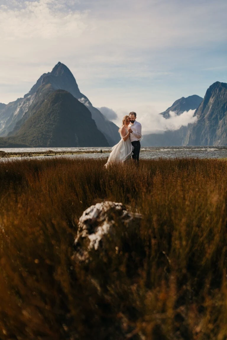 A bride and groom hold each other at Milford sound.