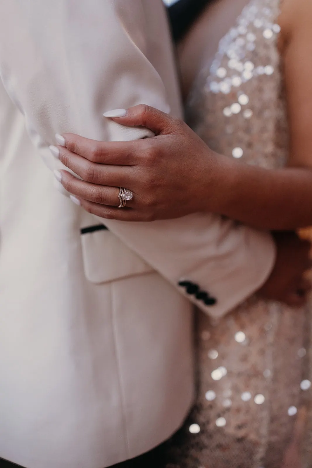 a close up detail photograph of an engagement ring while a couple holds each other closely