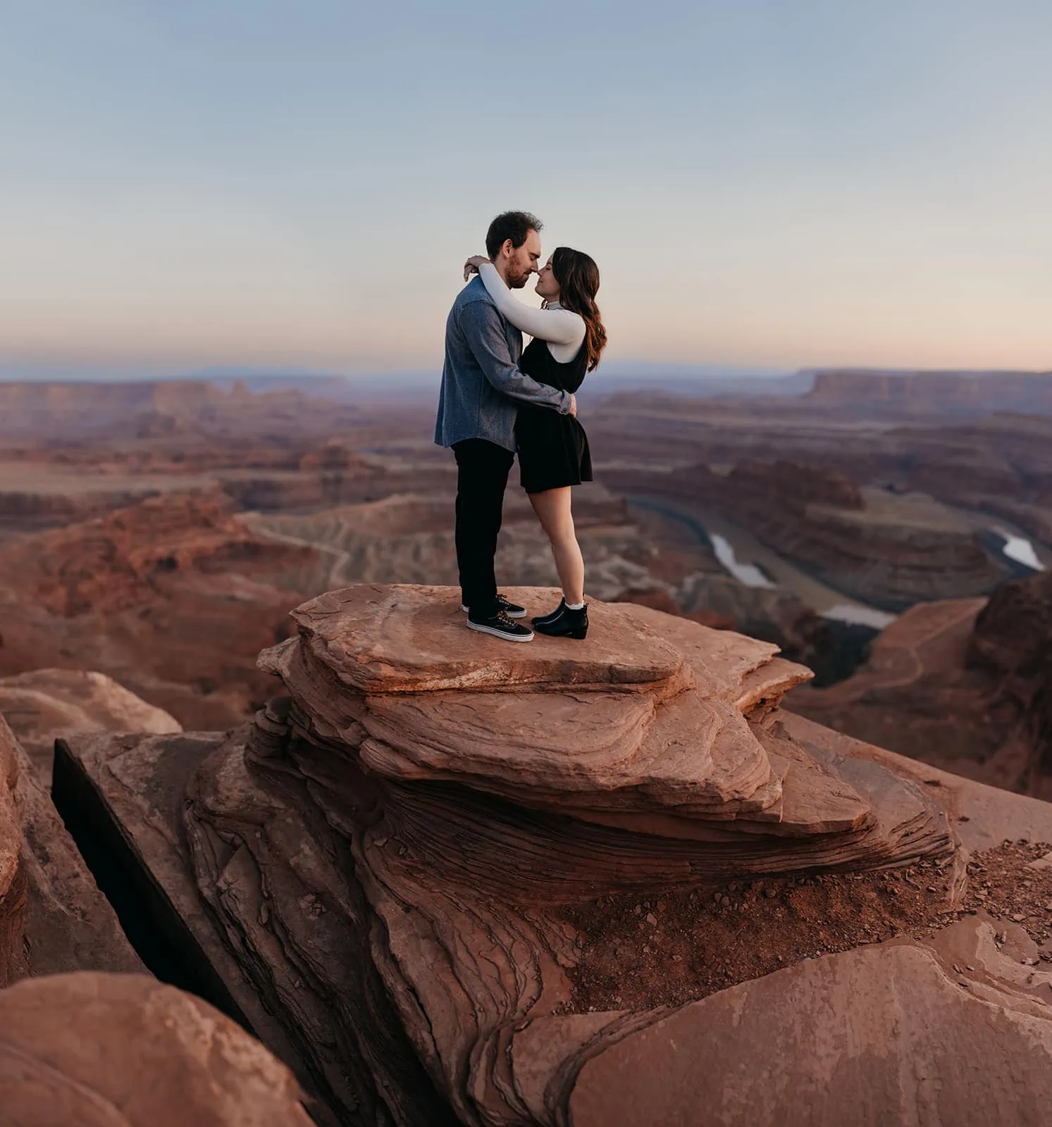 A man and woman share a kiss while up on a high vista ledge in Moab
