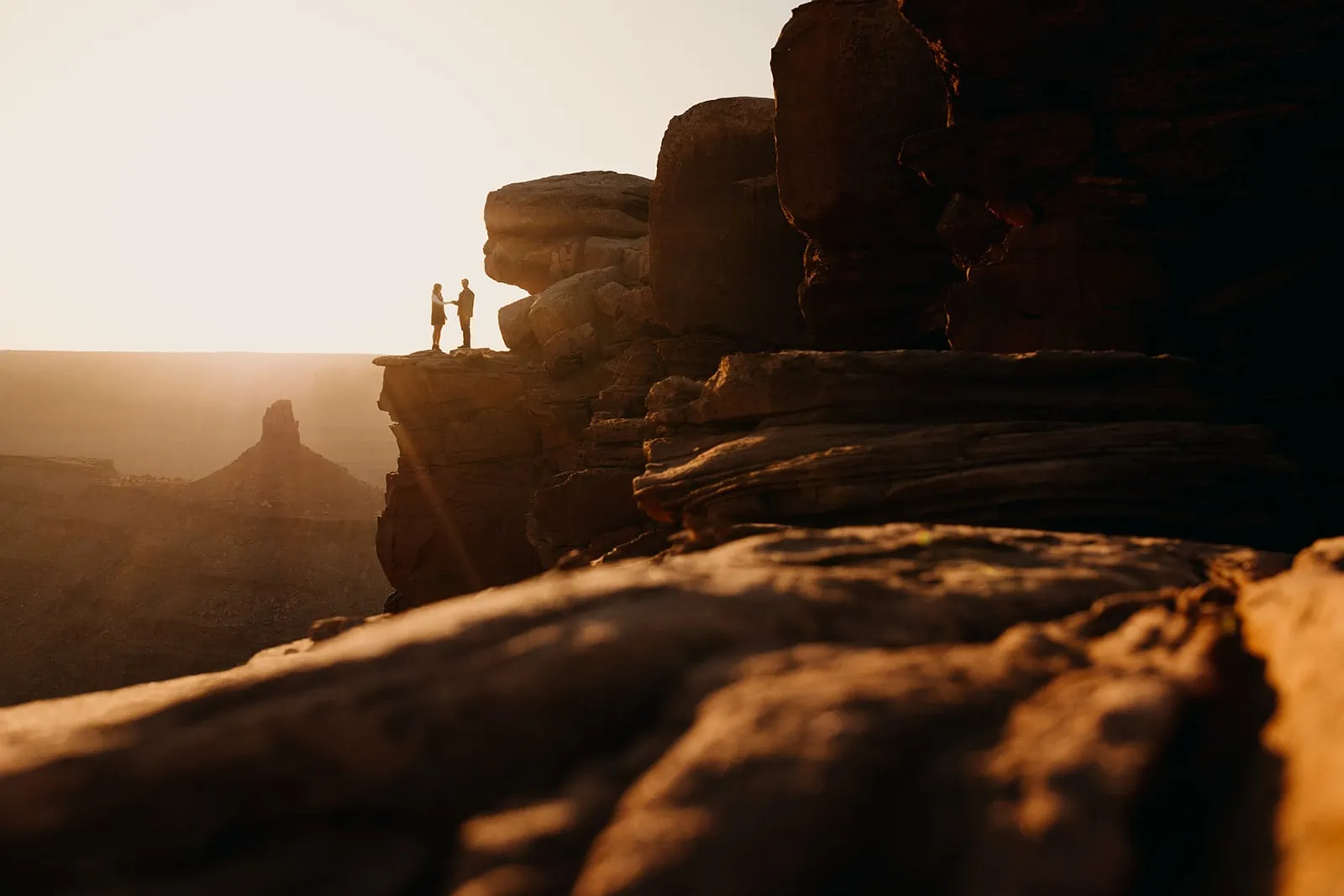 A man and woman stand together on a high up ledge at sunset in Moab