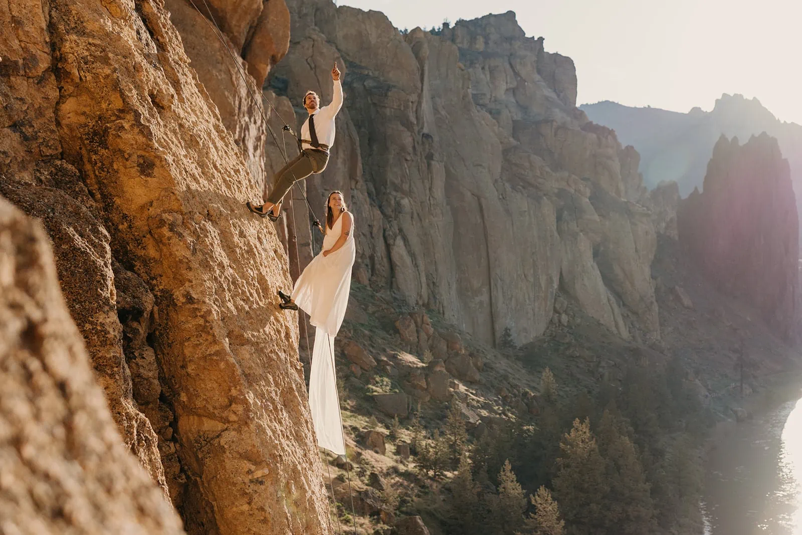 A couple climbs in Smith Rock State Park together at sunrise in their wedding attire.