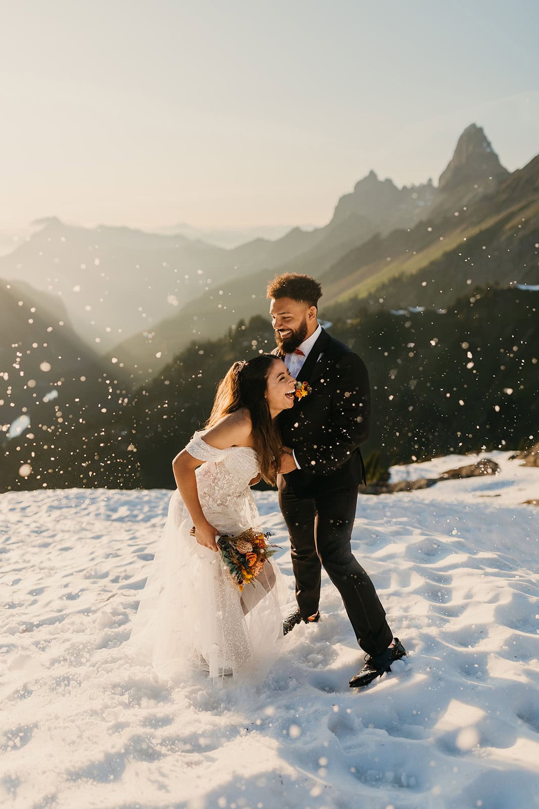 A couple laughs and plays in the snow during their summer mountain elopement. 