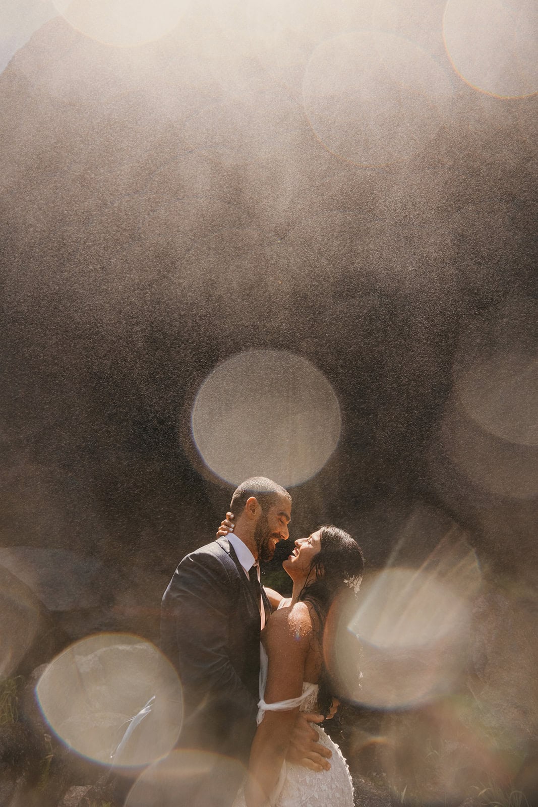 A couple laughs together under the powerful waterfalls in yosemite on their wedding day.