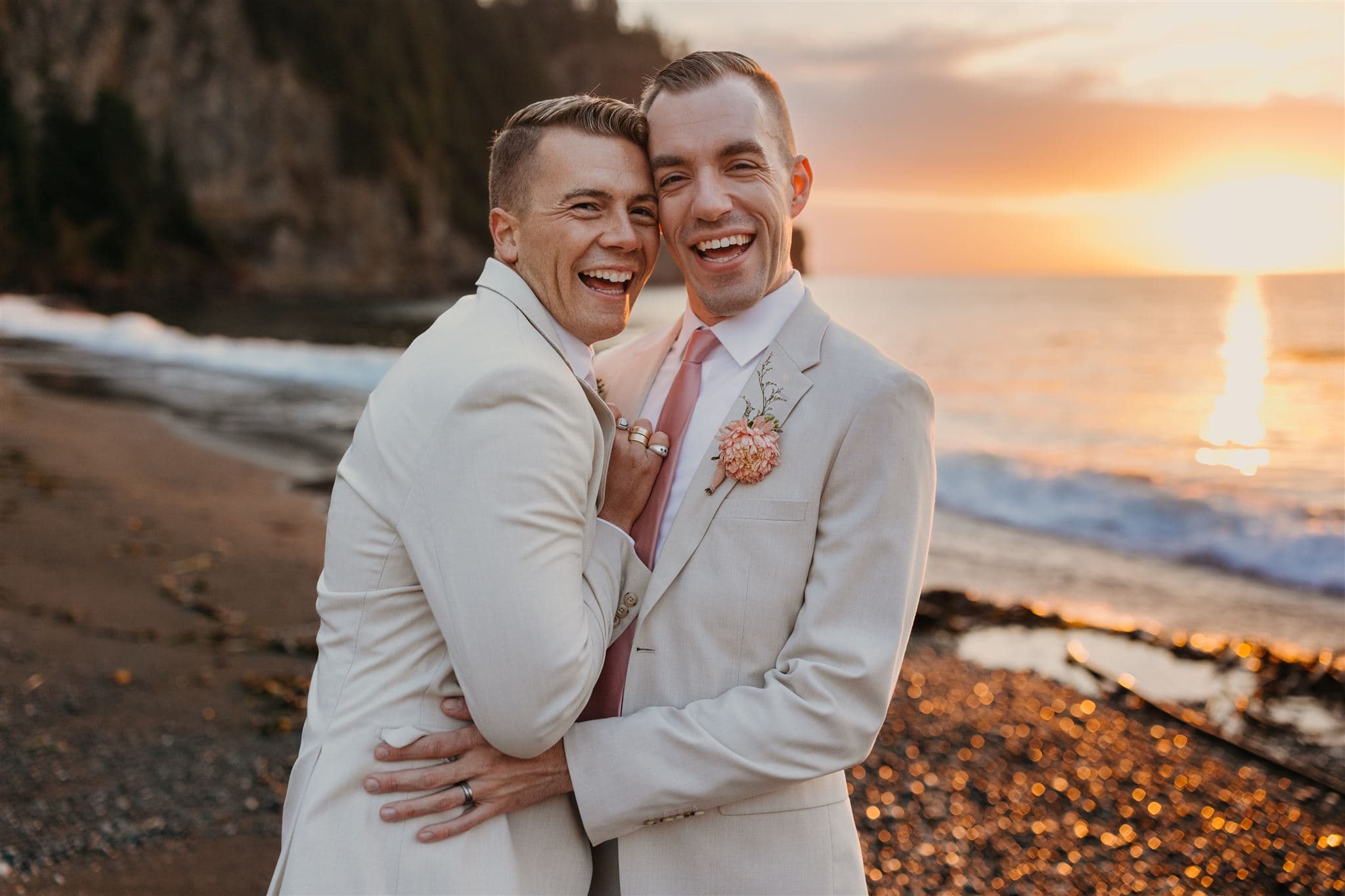 Two grooms smile and laugh during sunset portraits at Agate Beach Lodge.