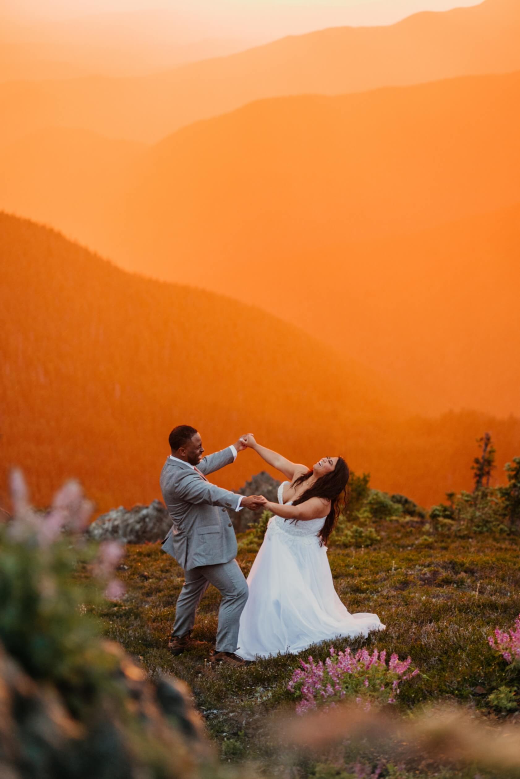 Two people dance happily under an orange sky on their elopement day.