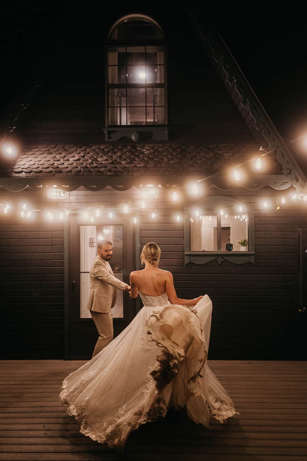 A bride and groom dance together with string lights and the A frame cabin behind them.