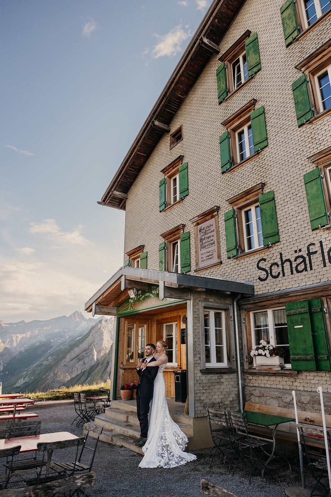 A bride and groom hold each other in front of a mountain hut.