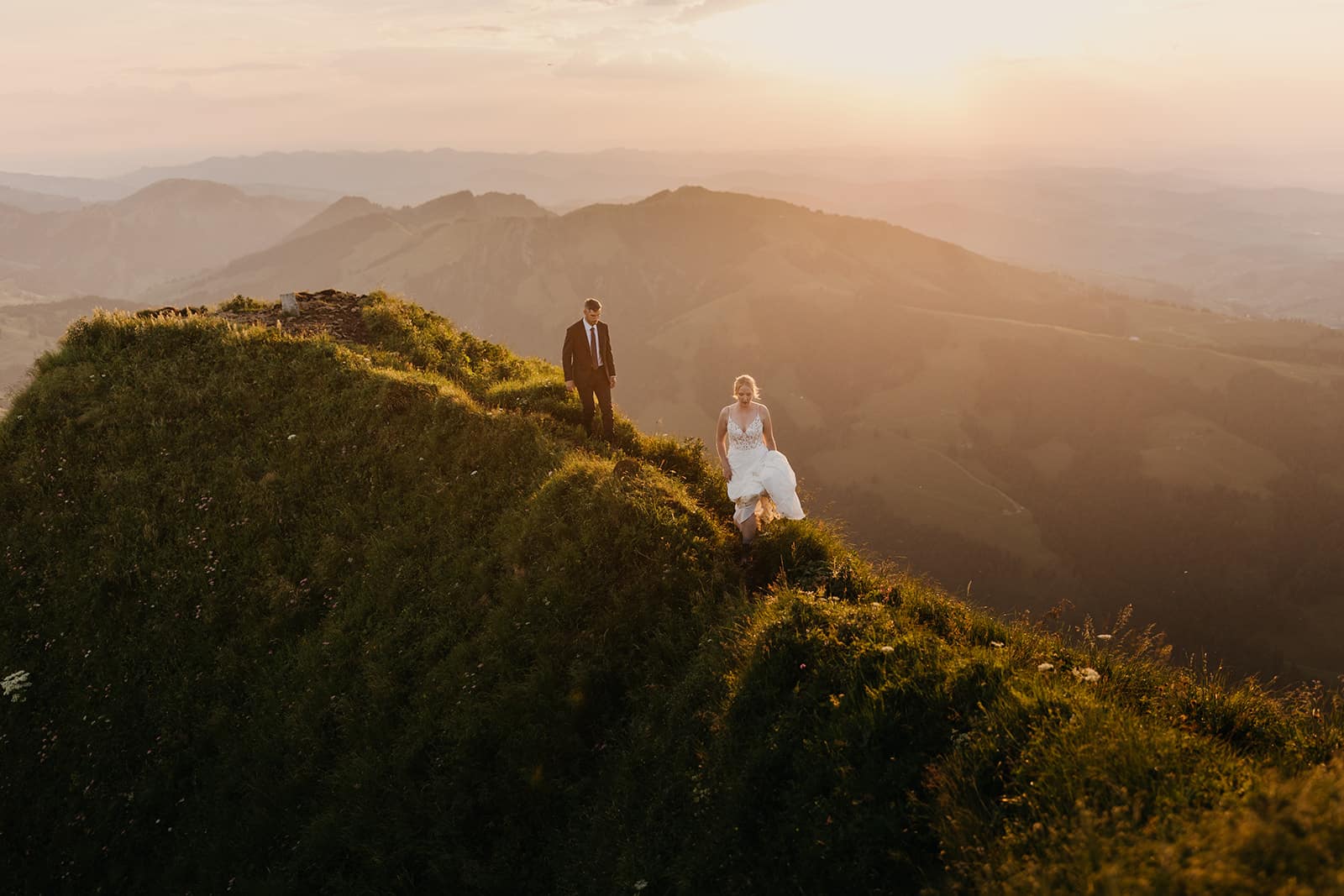 A couple walks along a ridge trail in the glowing sunset light.