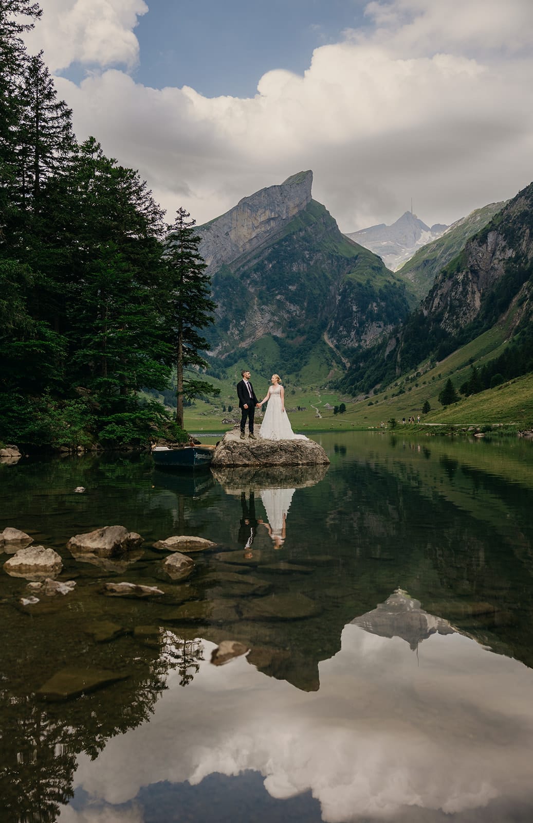 A couple stands on a rock in the middle of a lake.