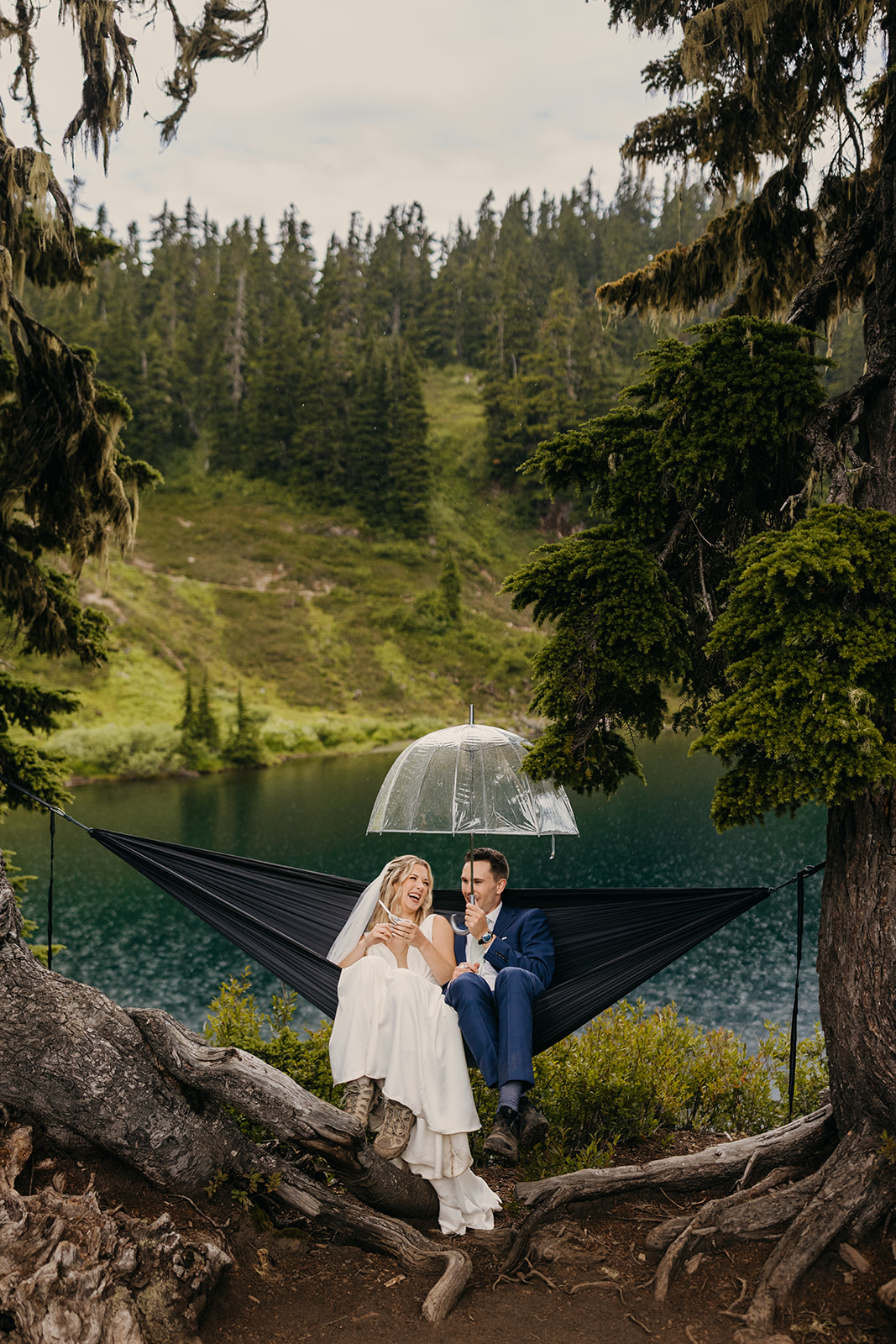 A couple sits together on a hammock with an umbrella in the rain