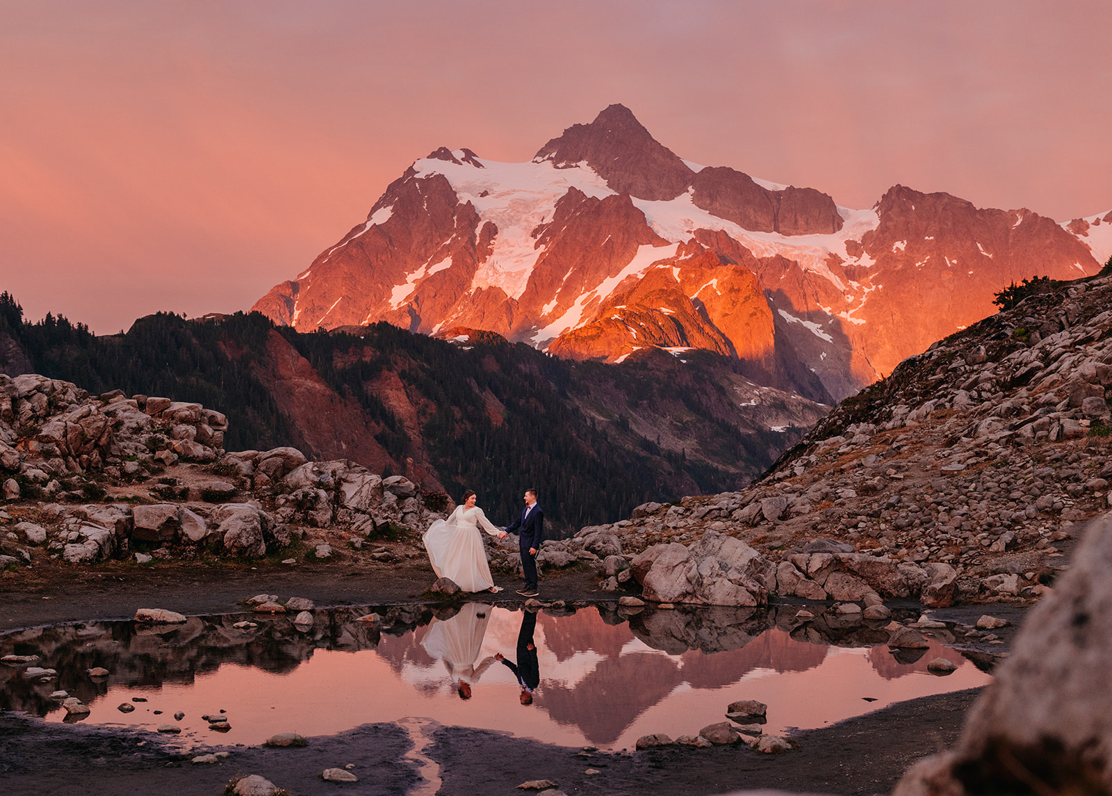 A couple stand together with the alpine light cast on Mt. Shuksan at sunset.
