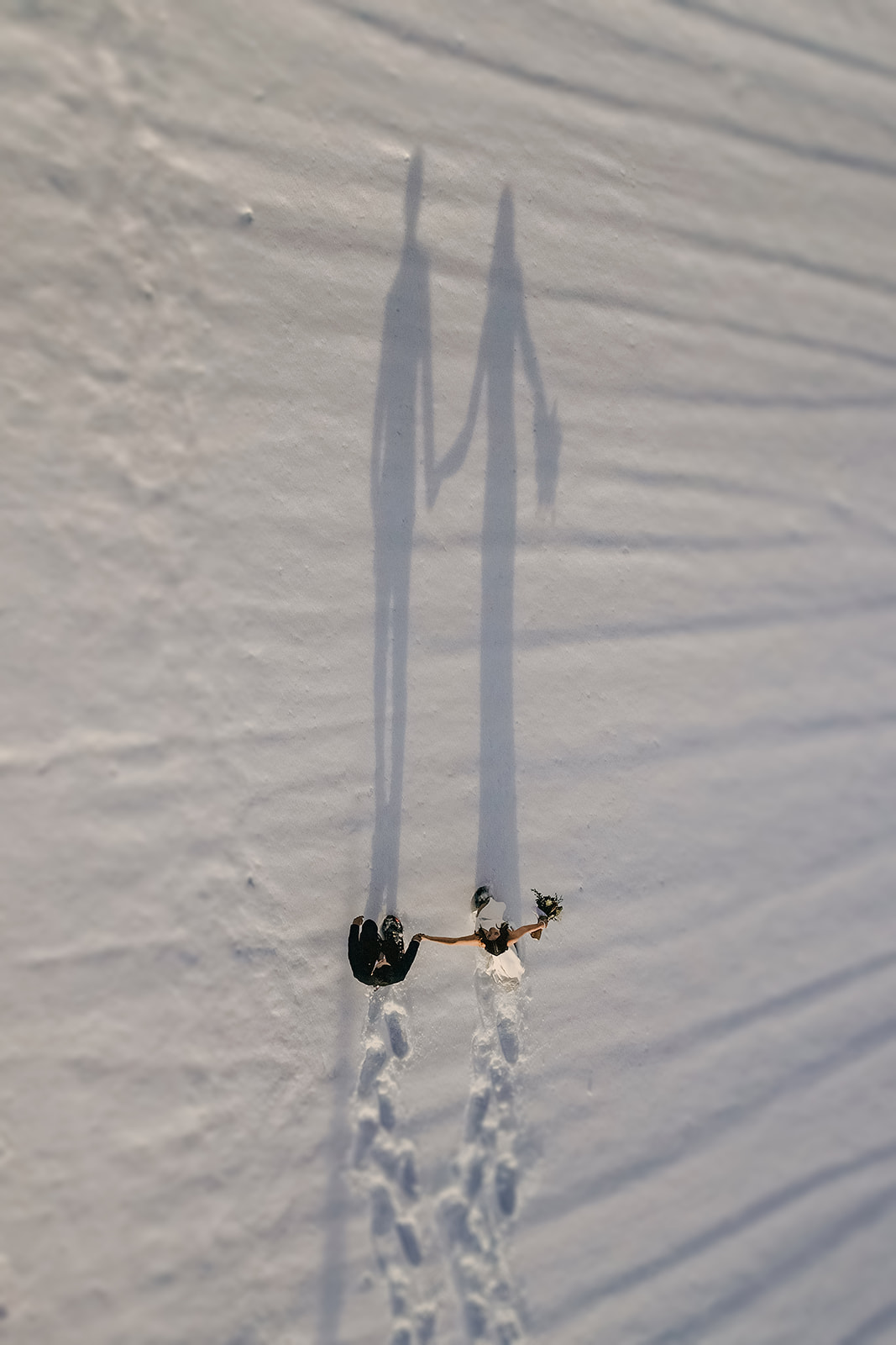 A wedding couple walking together holding hands in the snow.