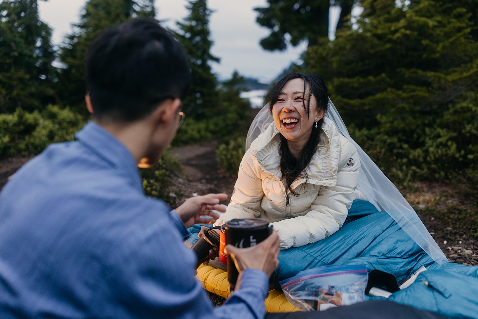 A bride laughs at her groom as they make their breakfast at their back country camp.