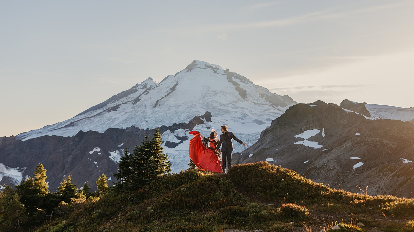 Bride wears red wedding dress on mountain trail during her backpacking elopement in the Mt Baker wilderness.