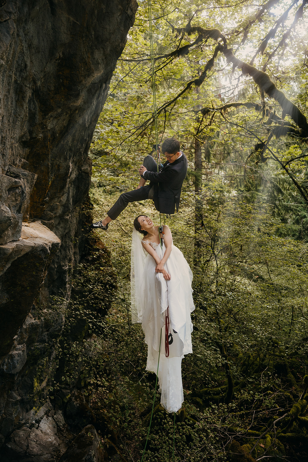 A bride and groom playfully rappelling on ropes together.