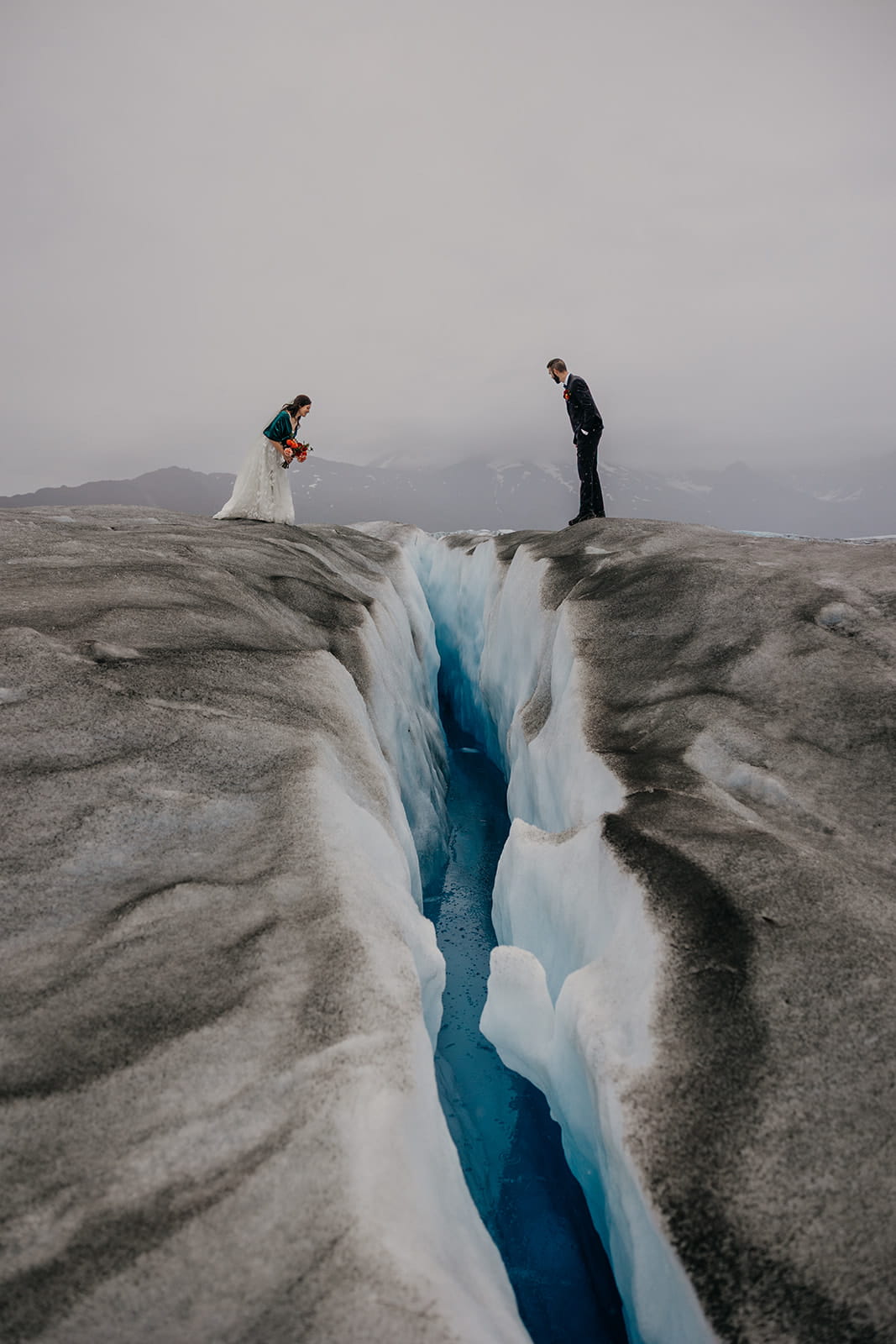 Bride and groom stand on opposite sides of a glacier split during their Alaska glacier elopement.
