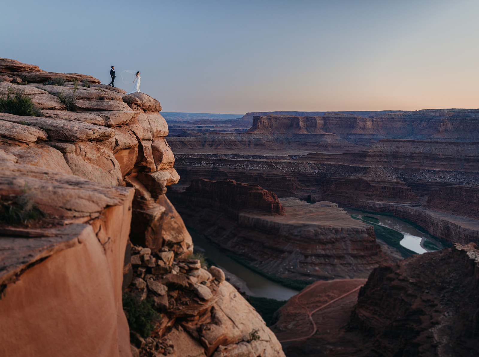 A wedding couple standing together on the edge of a cliff at Dead Horse Point State Park during blue hour