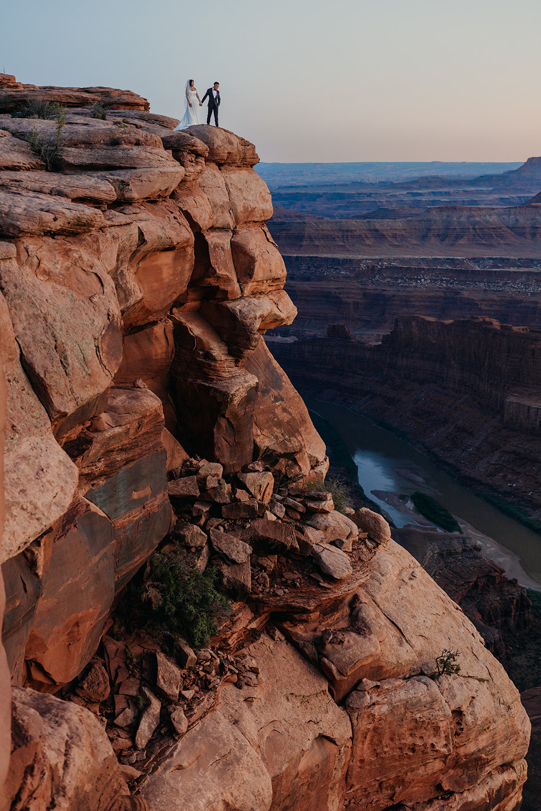 A wedding couple standing together on the edge of a cliff at Dead Horse Point State Park during blue hour
