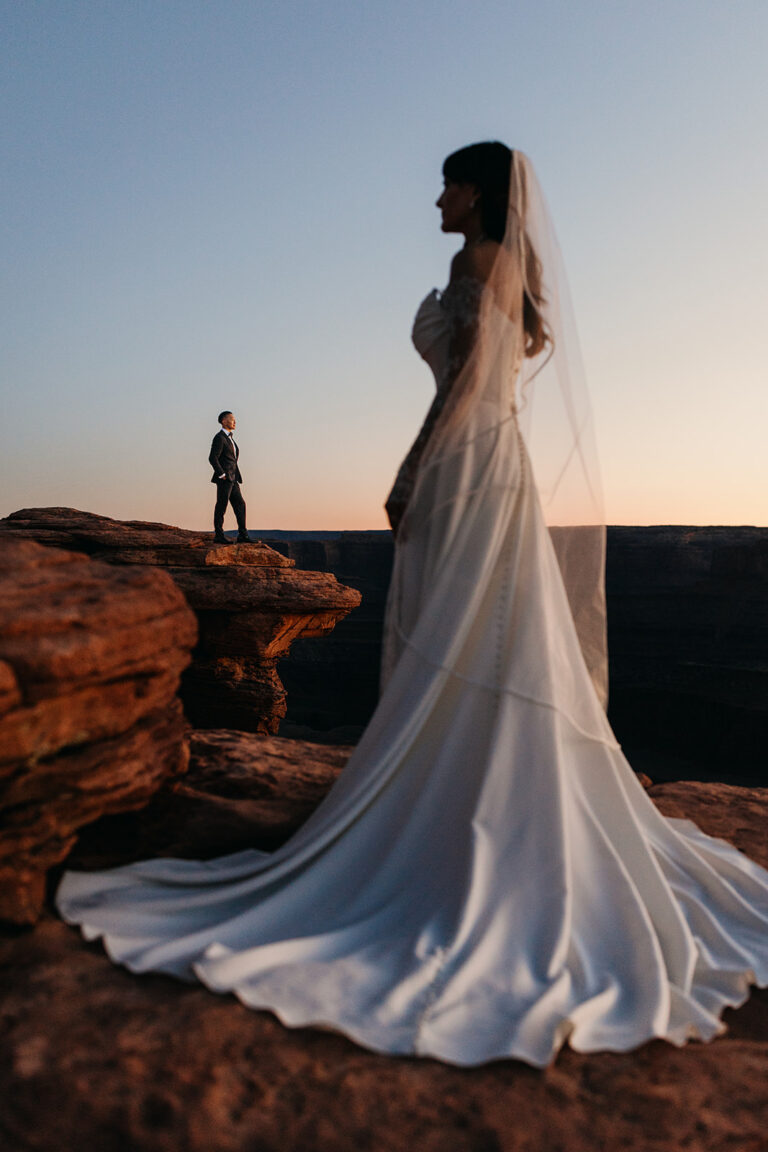 A bride looks toward her groom as they explore the cliff edges at sunset on their elopement day.