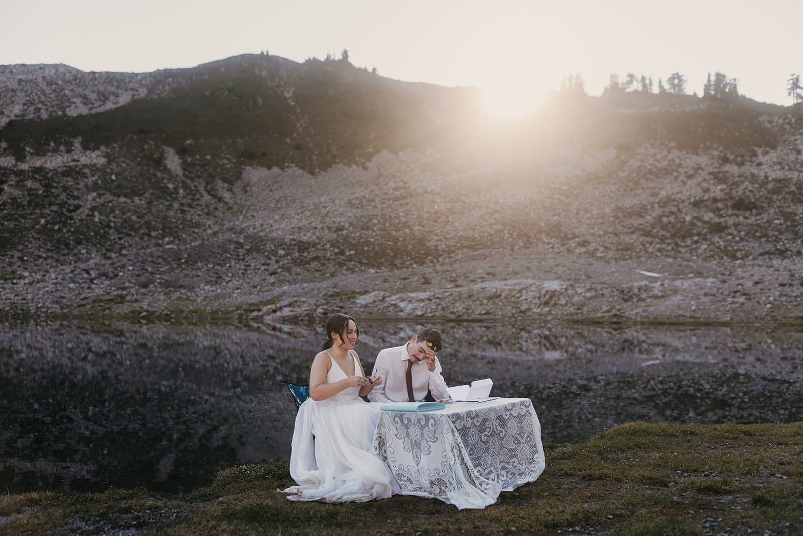 Bride and groom sit in camping chairs at the edge of Lake Ann to read letters from family.