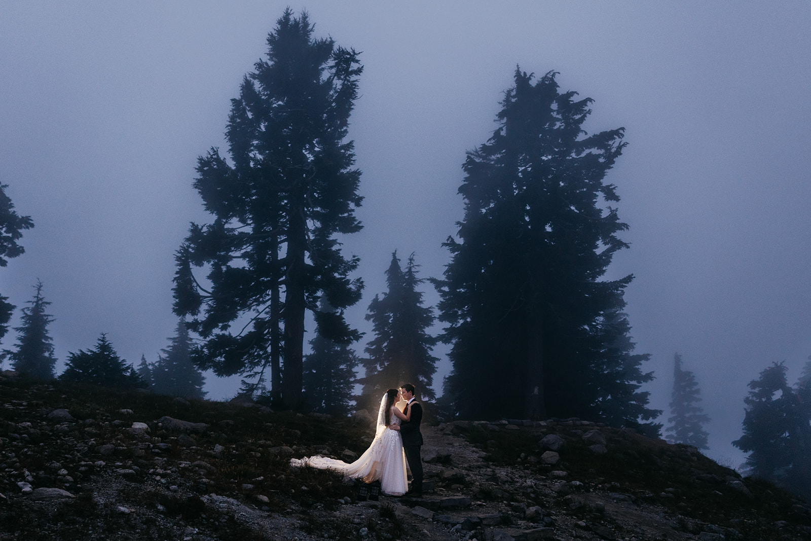 Newlyweds stand on a mountain trail during blue hour during their mountain elopement.