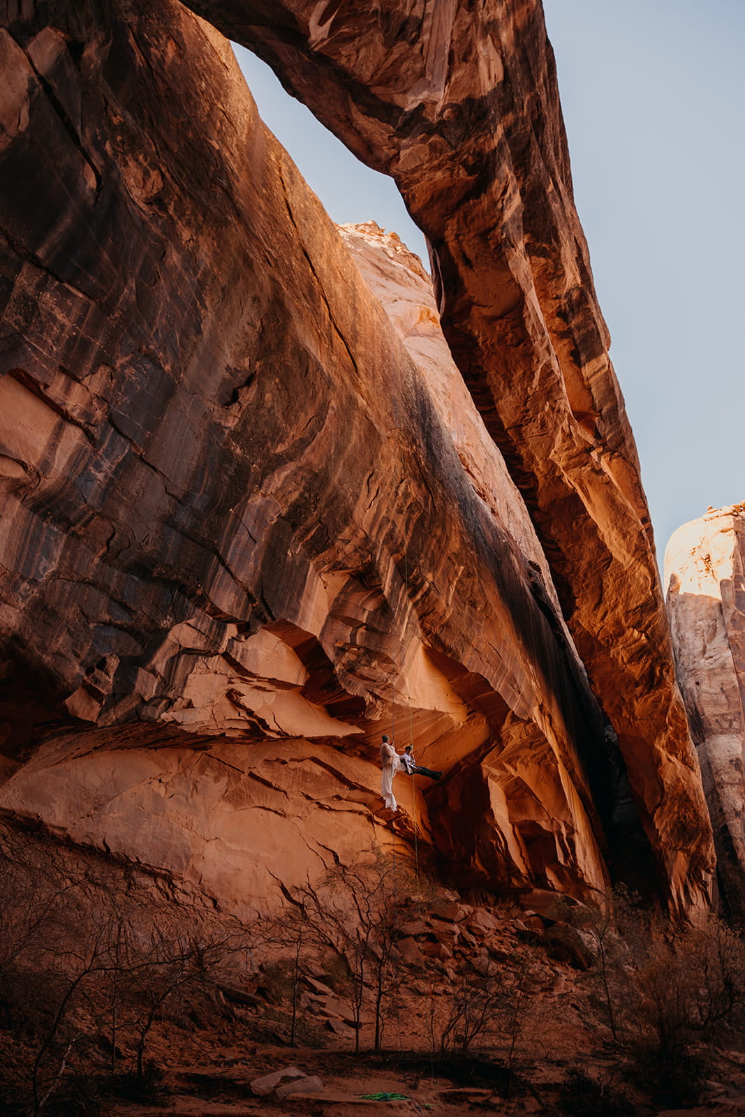 Newlyweds rappel a red rock wall during their winter elopement in Utah.