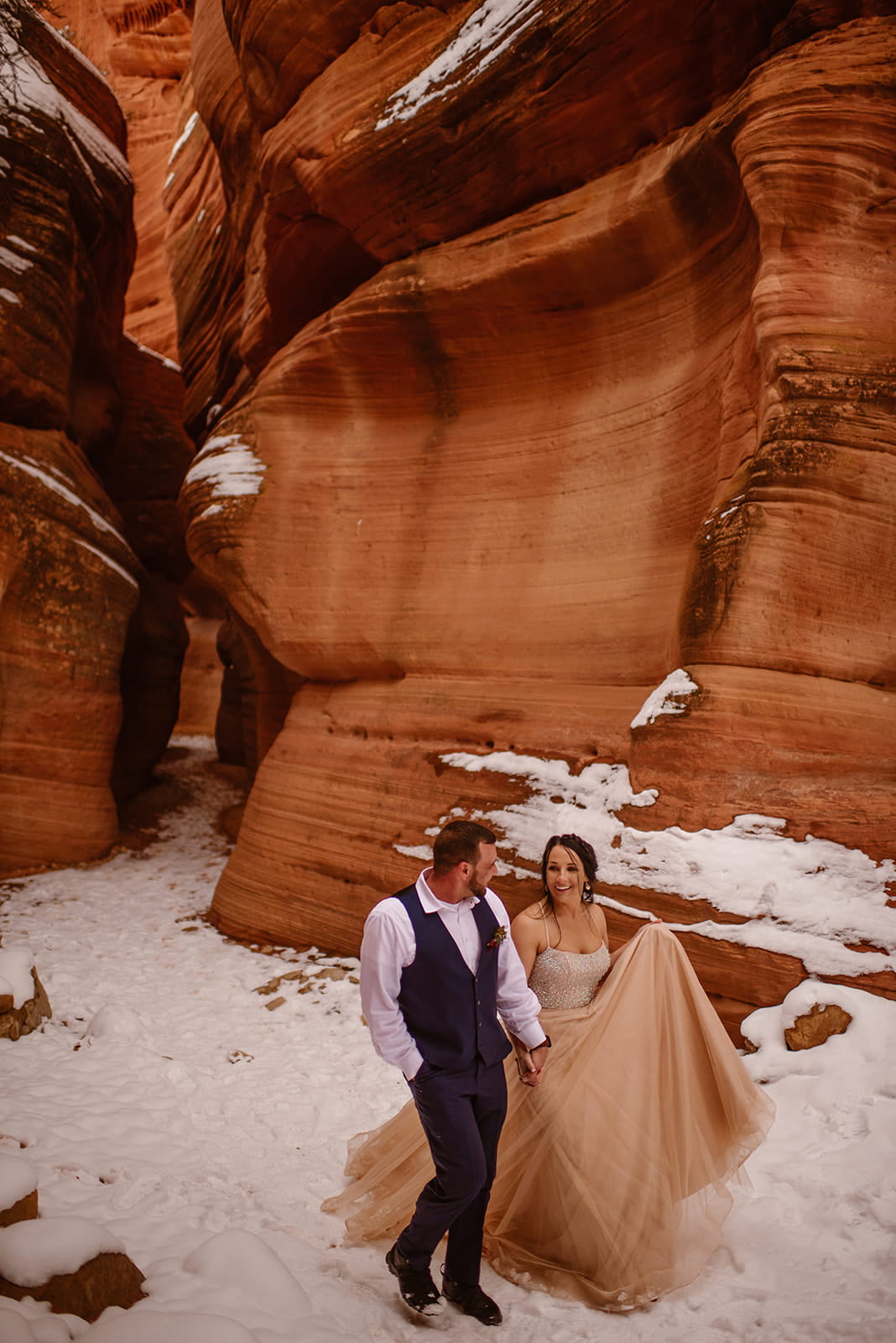 Newlyweds hold hands while walking through a snowy slot canyon during their winter elopement in Moab, Utah.
