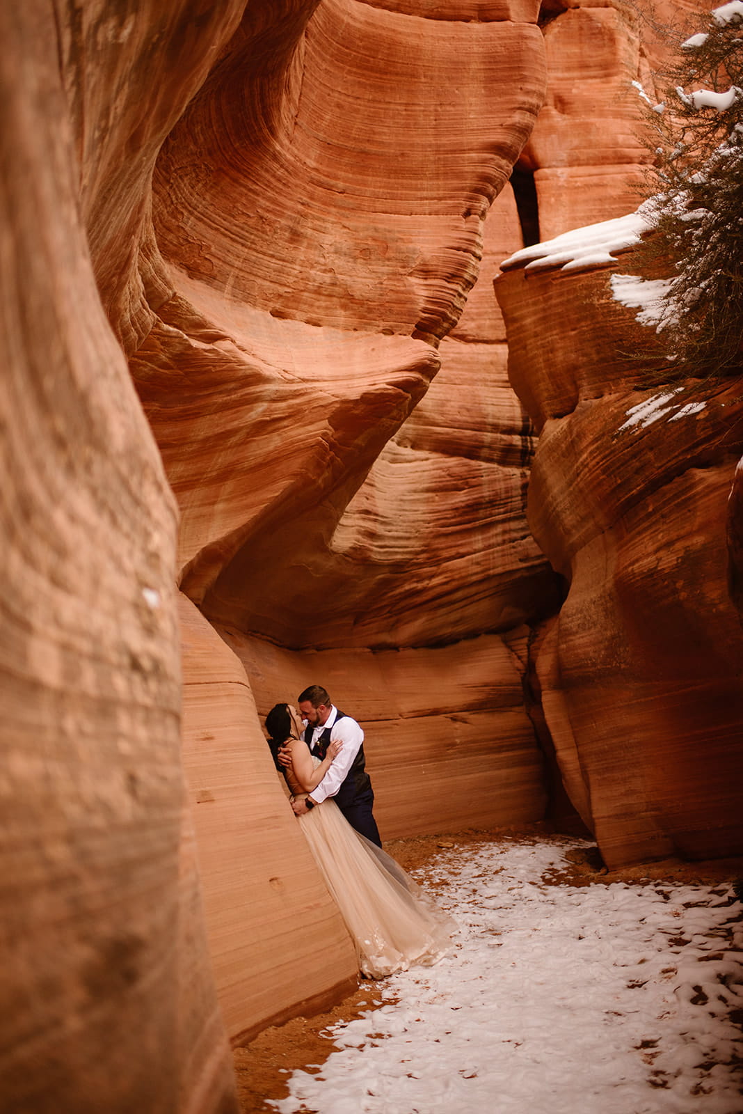 Newlyweds lean against the red rock walls during their winter elopement in Moab, Utah.