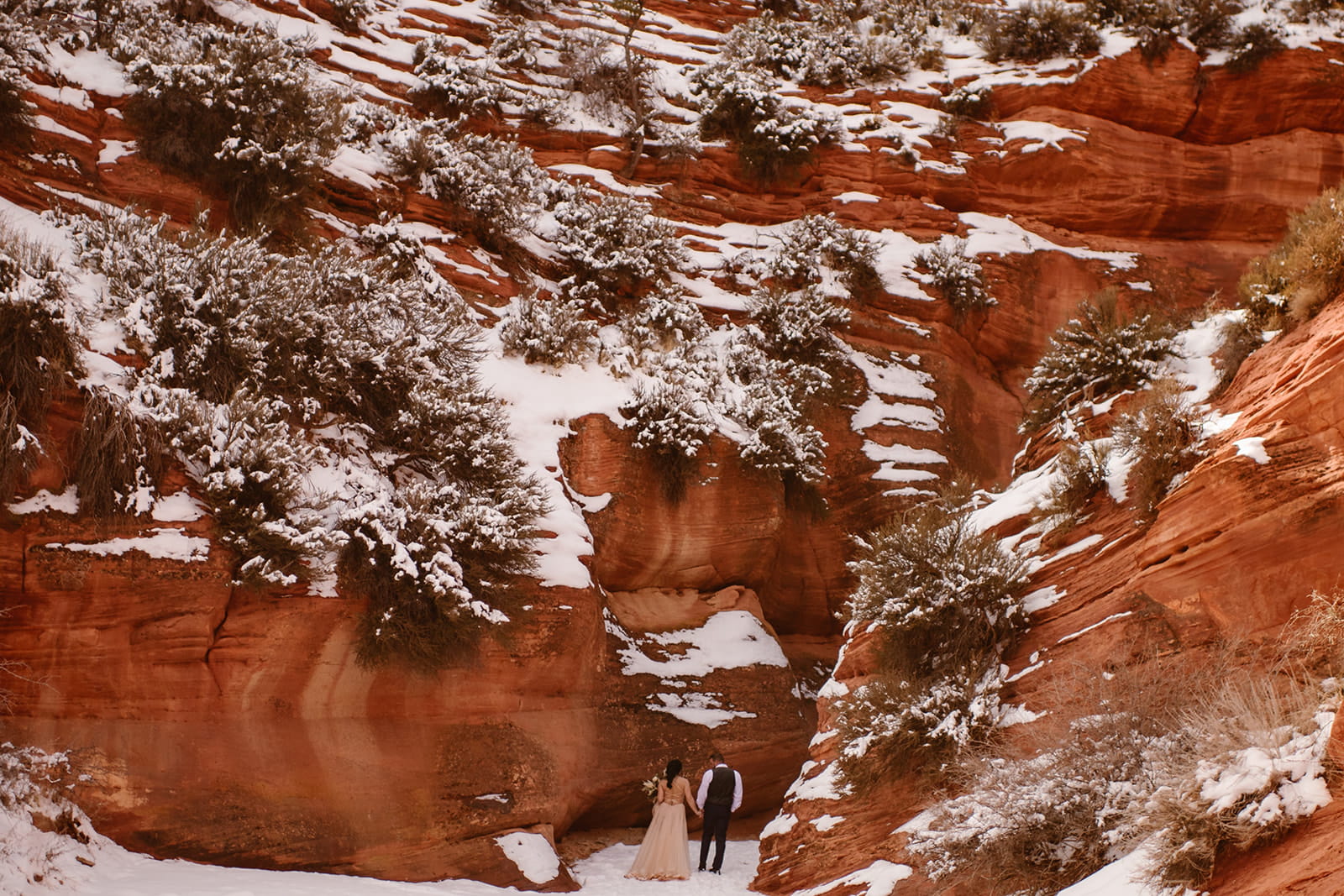 Bride and groom hold hands while entering a snowy red rock slot canyon during their Moab, Utah winter elopement.