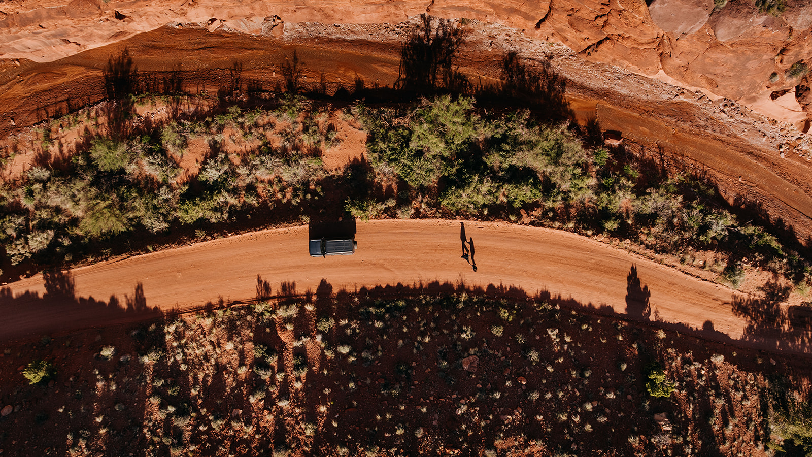 A couple walks along a  red dirt road together on sunny day as they off road through Moab's canyons.