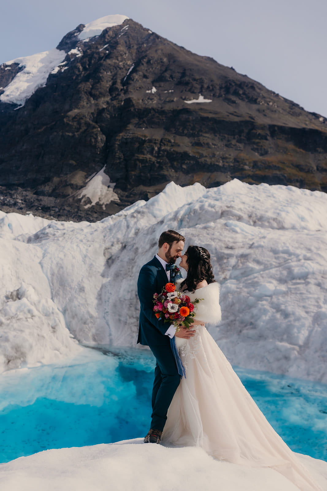 Newlyweds stand on the edge of an ice glacier during their destination wedding in Alaska.